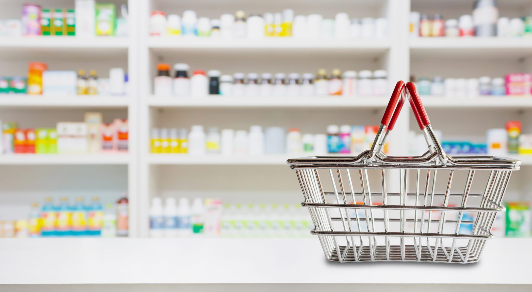 Empty shopping basket on pharmacy drugstore counter with blur shelves of medicine and vitamin supplements background